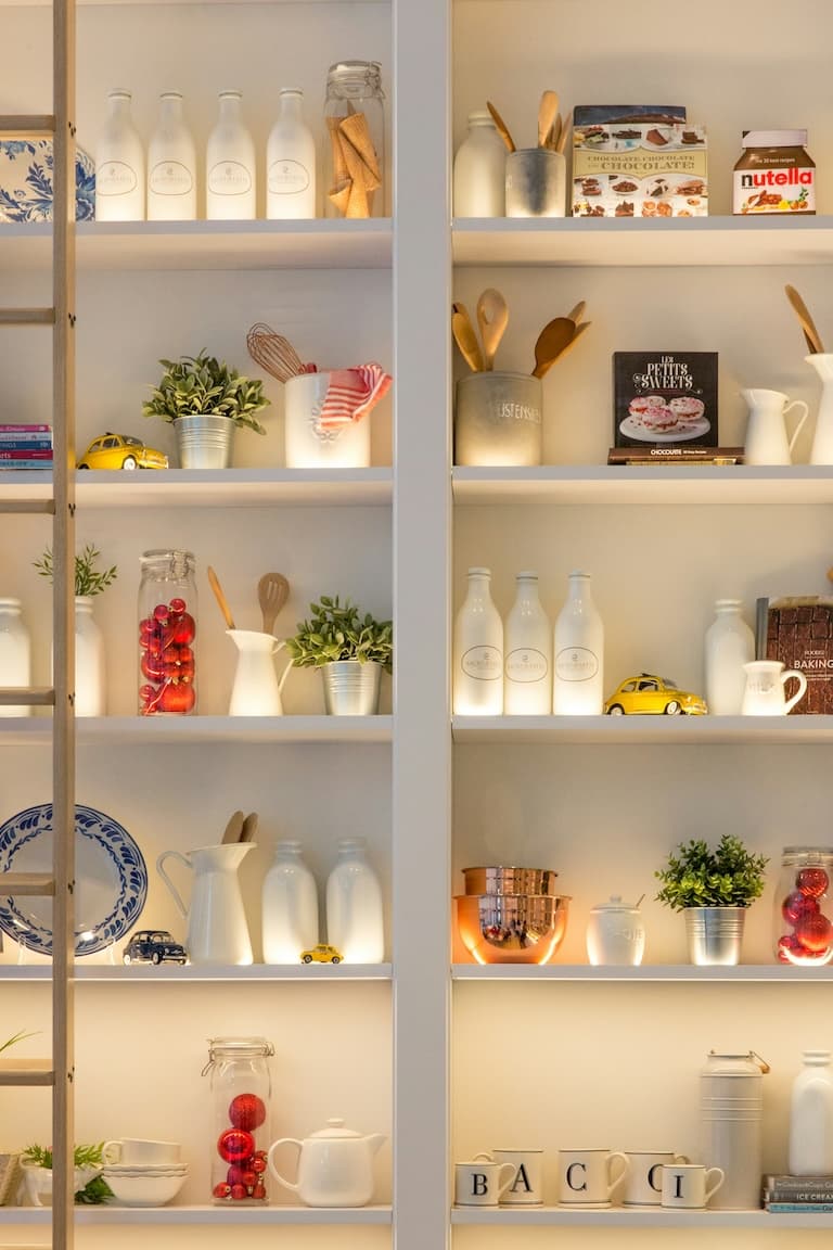 Warm backlit open kitchen shelving with bottles, plants, and ceramics